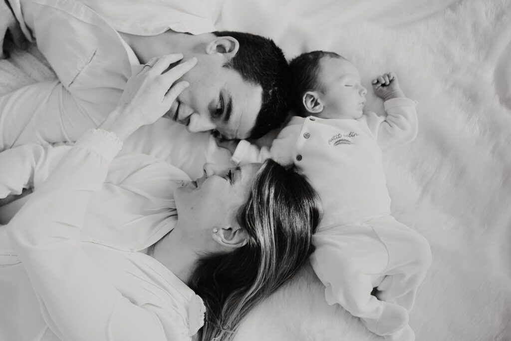 parents et leur nouvea-né allongés sur le lit. photos à domicile en noir et blanc
